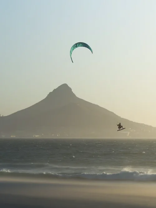A kitesurfer in the air off Blouberg with Lion's Head across the bay