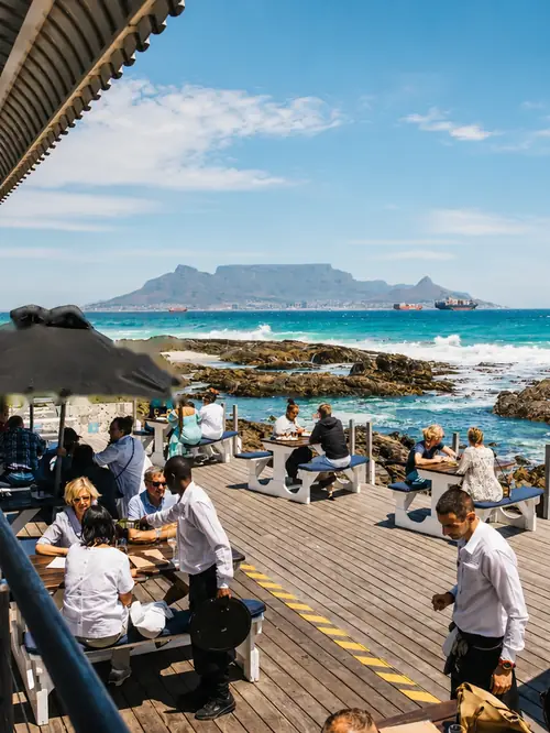 Diners on a timber deck above the rocks, Table Mountain across the bay