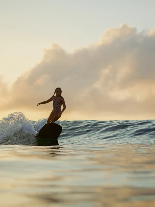 A surfer riding a wave at sunset off the Cape coast